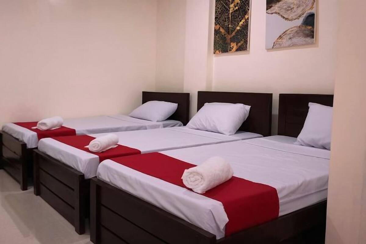 Una habitación de hotel con tres camas individuales, cada una con una colcha roja y almohadas blancas.