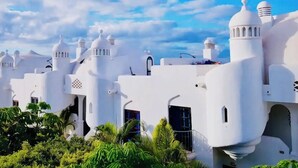 Un edificio blanco con múltiples cúpulas y torres, rodeado de exuberante vegetación.