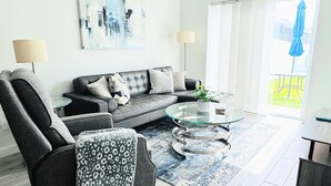 Un salon moderne avec un canapé gris, une table basse en verre et un fauteuil à motifs.