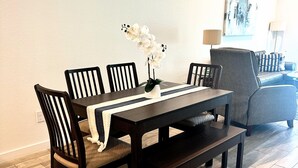Un coin repas avec une table en bois foncé, quatre chaises, un banc et une orchidée blanche en guise de centre de table.