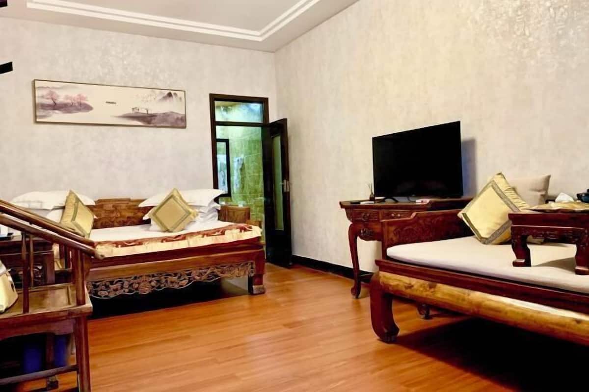 Una habitación de hotel con cama, televisión, mesita de madera y un cuadro en la pared.