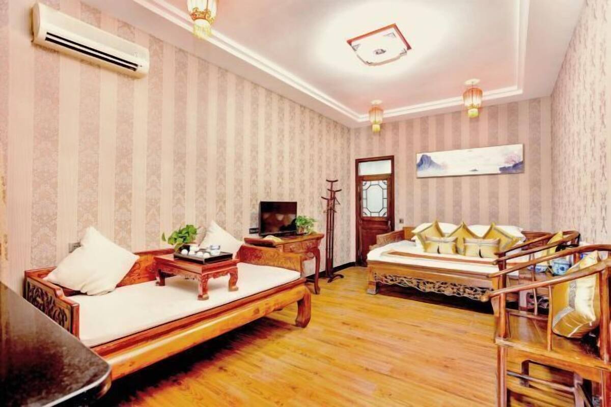 Una habitación con sofá, cama con almohadas, una mesita con planta, televisor y aire acondicionado instalado en la pared.