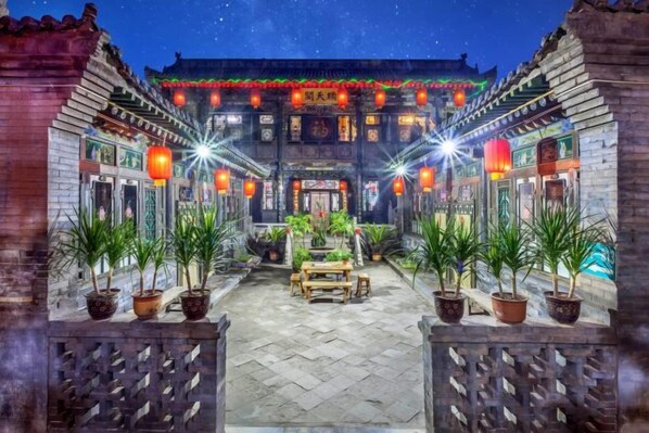 A traditional courtyard with potted plants, a wooden bench, and illuminated lanterns.