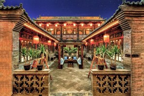 A traditional courtyard with a central seating area, surrounded by brick walls and potted plants.