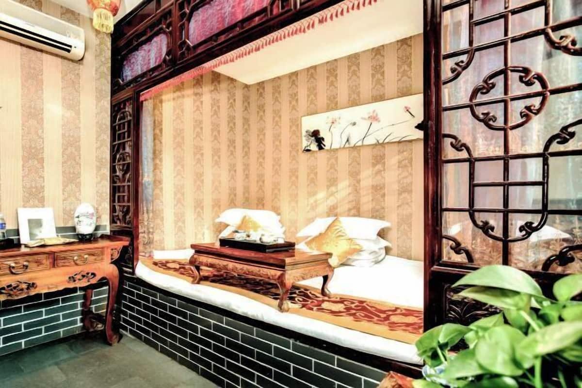 Una habitación tradicional con cama, cómoda de madera, escritorio y ventana con rejas decorativas de hierro.