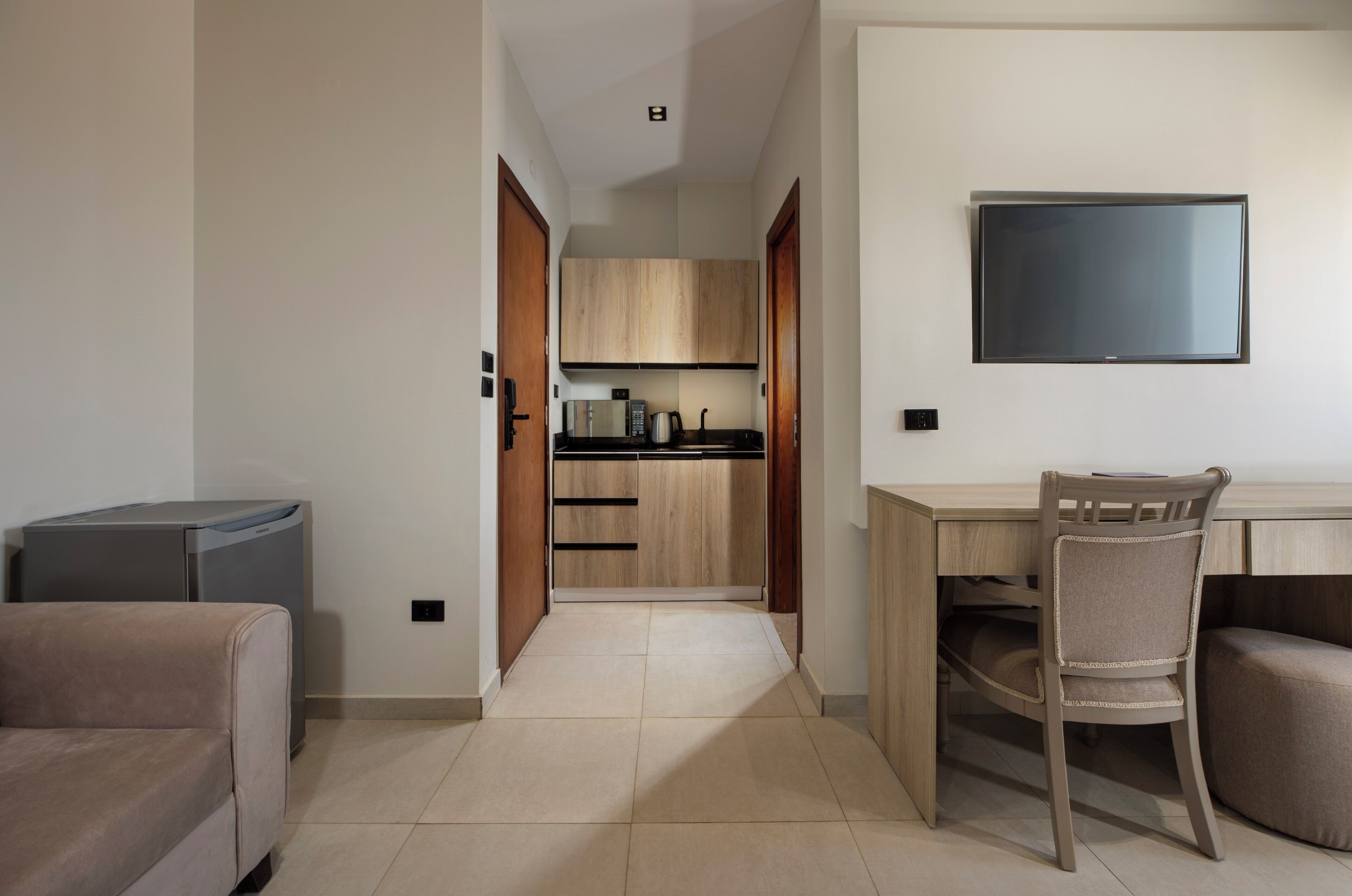 A modern kitchen with wooden cabinets, a built-in oven, and a flat-screen TV mounted on the wall.