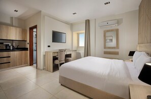 A hotel room with a bed, desk, chair, and kitchenette.