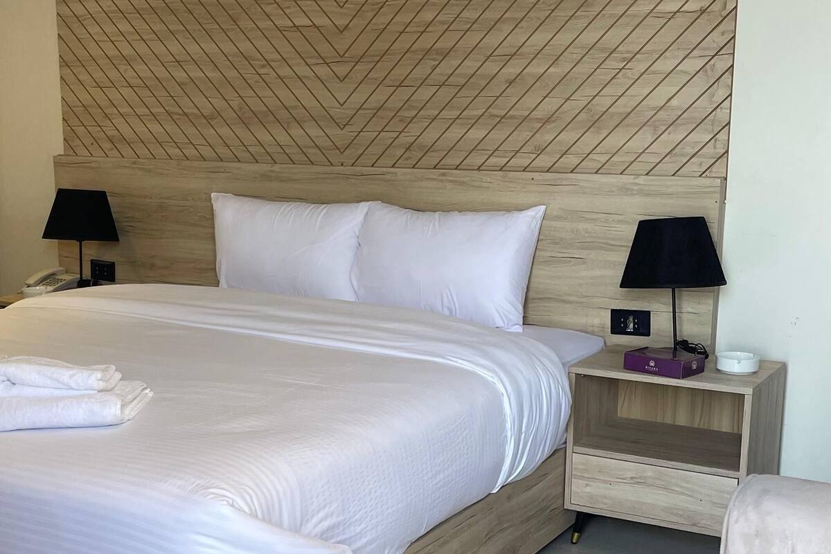 A hotel room with a large bed, two bedside tables, and a headboard with a geometric pattern.