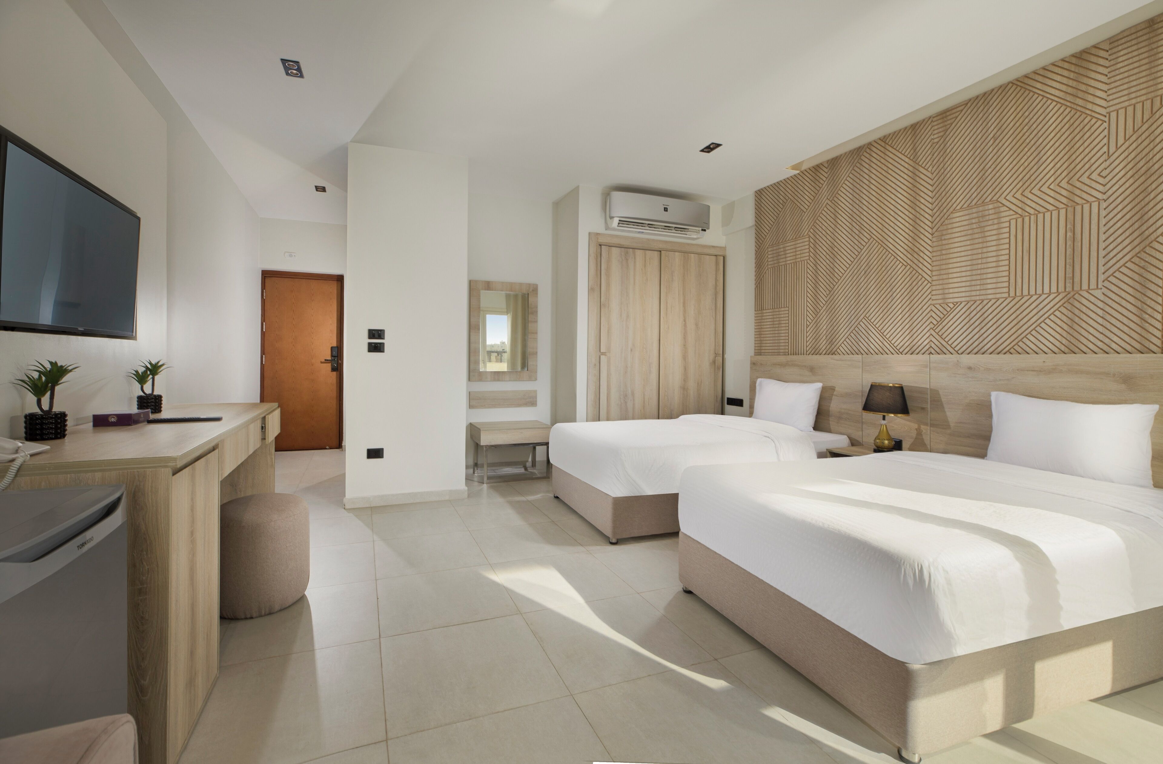 A modern hotel room with two beds, a desk, a TV, and a wardrobe.