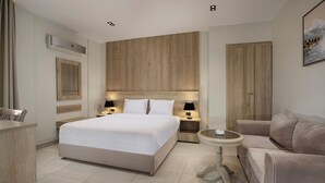 A modern hotel room with a large bed, bedside tables with lamps, a round table, a sofa, and a wooden headboard. - Rivana Residence New Cairo - Pool & GYM Access (New Cairo)