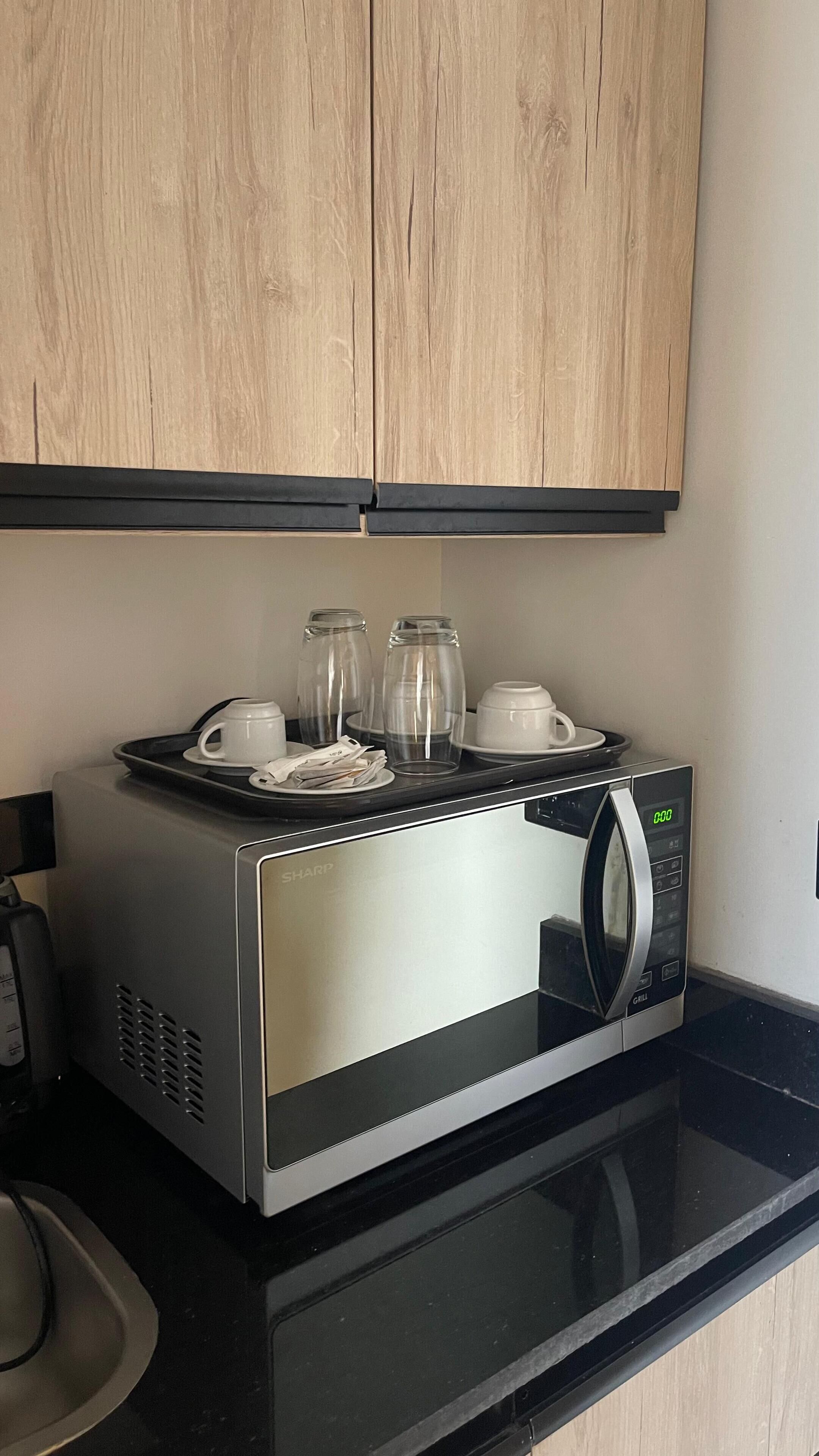 A kitchen with a microwave, a tray with cups and a plate, and a coffee maker.