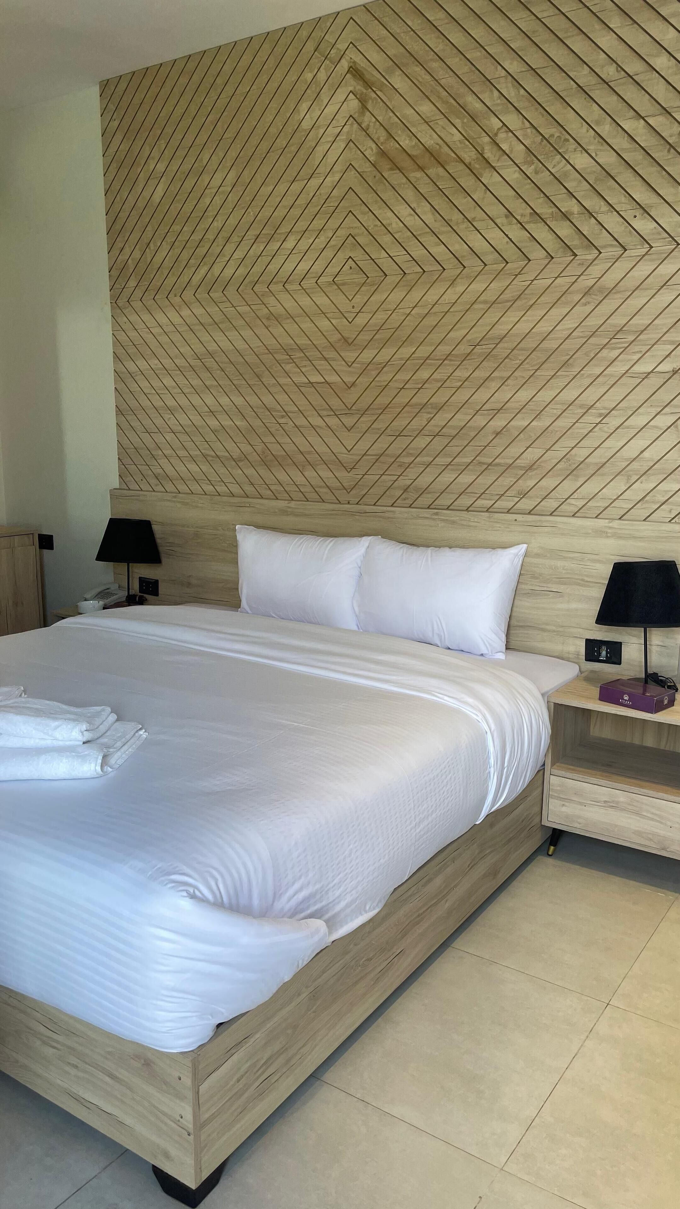 A neatly made bed with white linens, a wooden headboard with a geometric pattern, and two bedside tables with lamps.
