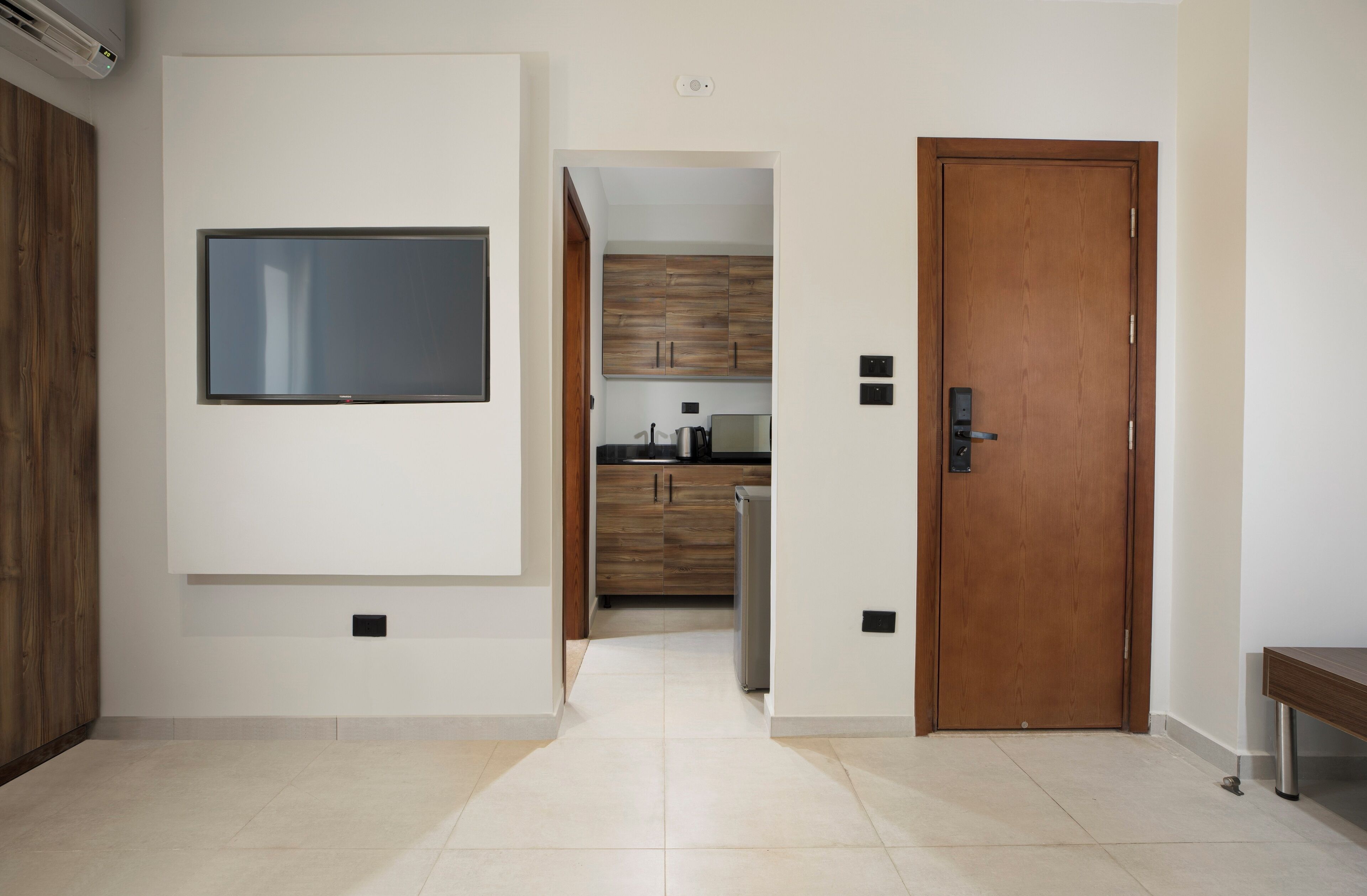 A modern living room with a flat-screen TV mounted on the wall, a wooden door, and a bench.