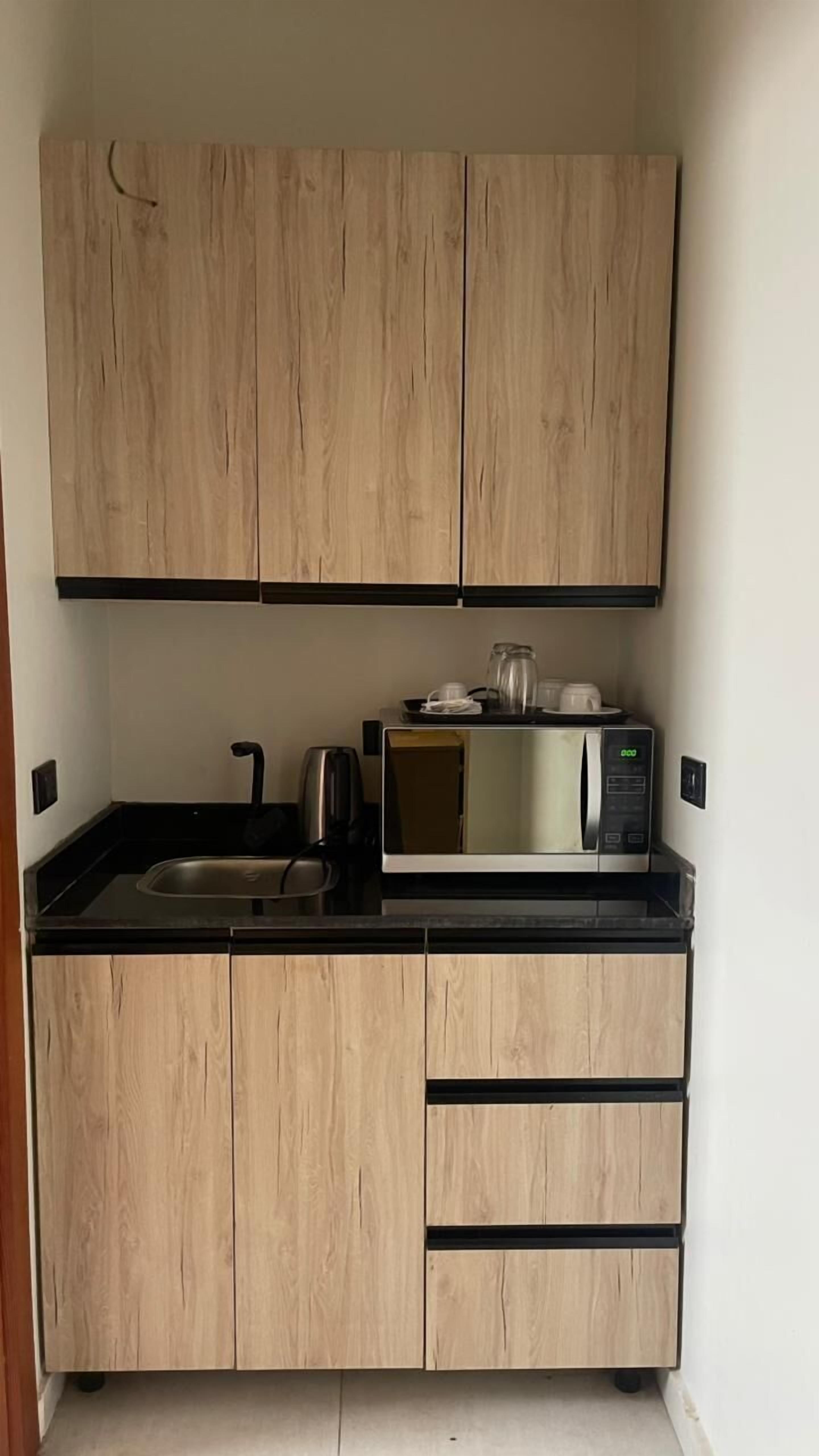 A compact kitchen with wooden cabinets, a black countertop, a microwave, and a kettle.