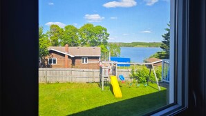 A view of a backyard with a wooden house, a yellow slide, and a body of water in the background.