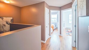Un pasillo con piso de madera, una puerta blanca que da a un dormitorio, y una lámpara en el techo.