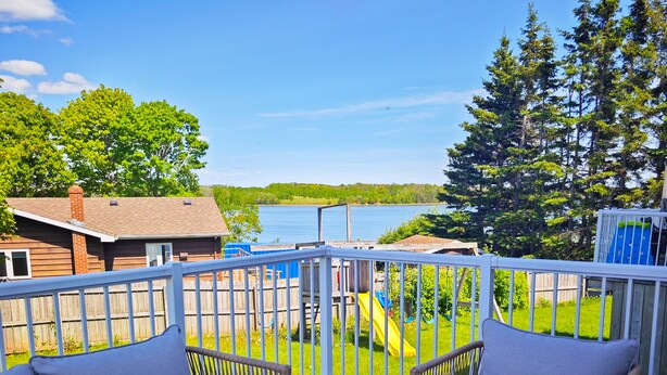 A balcony with a view of a lake, a wooden deck, and a play area in the background.