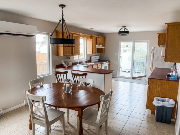 A modern kitchen with wooden cabinets, a dining area with a wooden table and chairs, and a sliding glass door leading to a balcony.