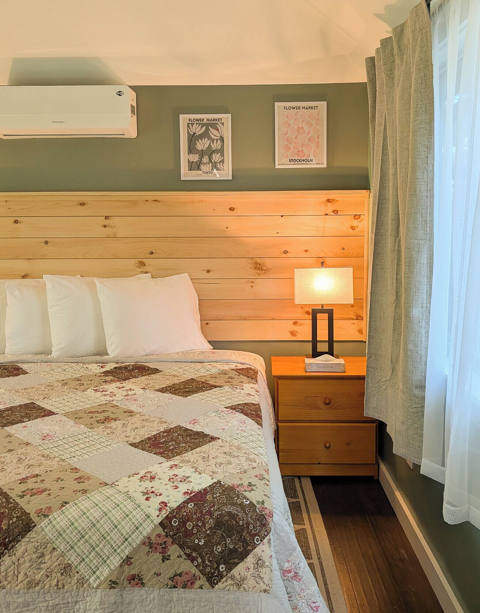 Une chambre à coucher avec une tête de lit en bois, une couvre-lit matelassée, une lampe de chevet et deux tableaux encadrés accrochés au mur.