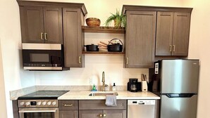 Una cocina moderna con armarios de madera oscura, electrodomésticos de acero inoxidable, horno empotrado, lavavajillas y cafetera.