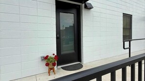 Un edificio moderno con fachada blanca, una puerta negra y una pequeña maceta con flores rojas en la planta baja.