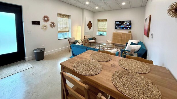Amplia sala de estar con una mesa de comedor de madera, sofás azules y un televisor montado en la pared.
