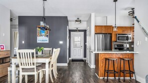 Une cuisine moderne dotée d’un îlot central, de meubles en bois, d’appareils électroménagers en acier inoxydable et d’un coin repas avec une table et des chaises blanches.