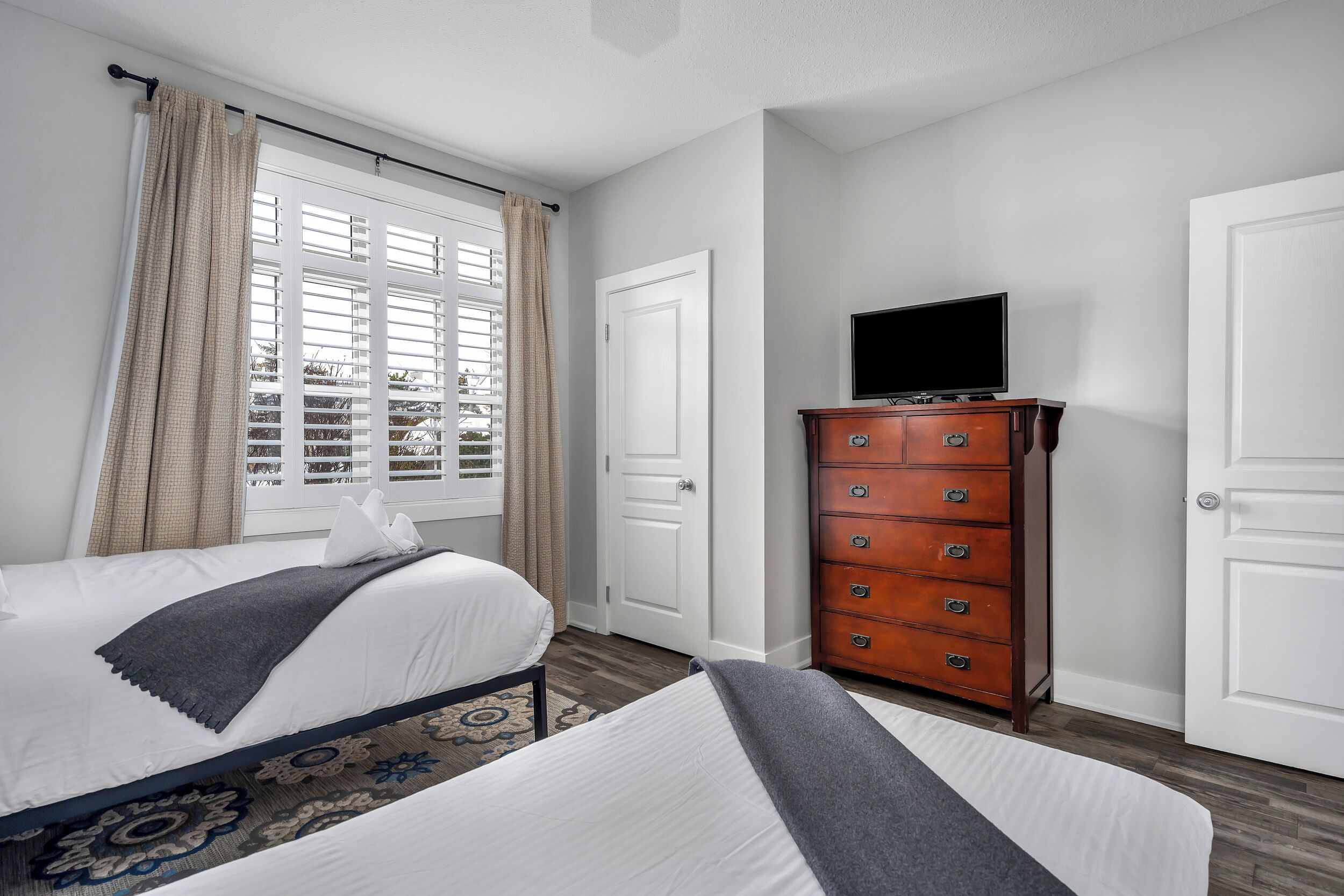 Habitación de hotel con cama, cómoda, televisor y ventana con cortinas.