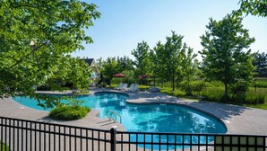 Une piscine à bord incurvé, entourée d’une clôture et ombragée par des arbres.
