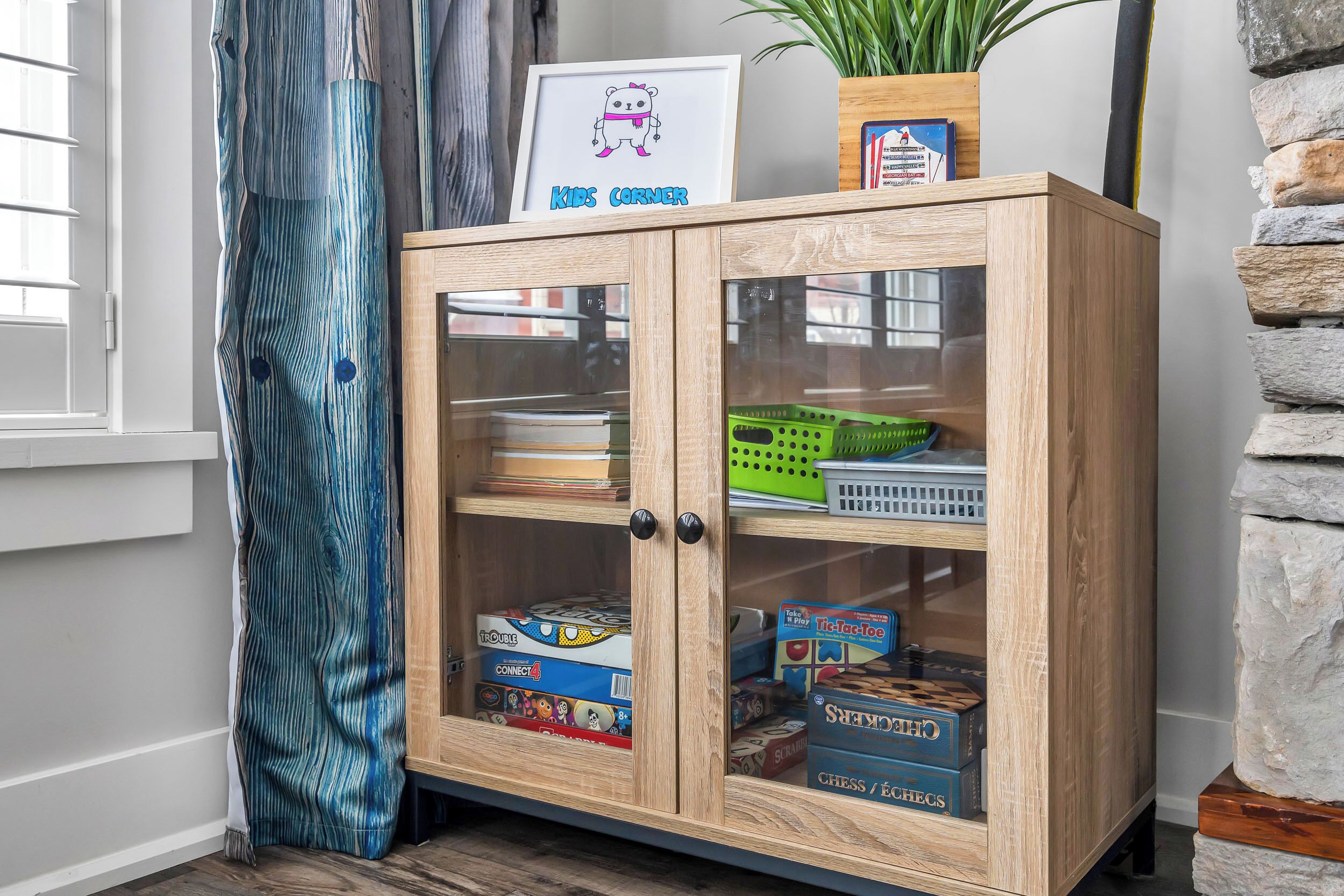 A wooden cabinet with glass doors containing board games and a framed picture labeled "Kids Corner".
