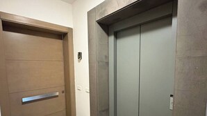 Un pasillo con una puerta de madera y un moderno ascensor.
