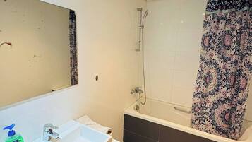 A modern bathroom with a white sink, a mirror, a shower with a glass door, and a patterned shower curtain.