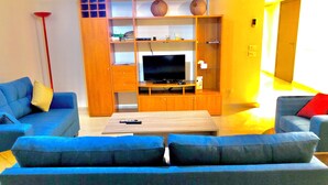 Una sala de estar con dos sofás azules, una mesa de centro y un mueble para televisión con televisor de pantalla plana.