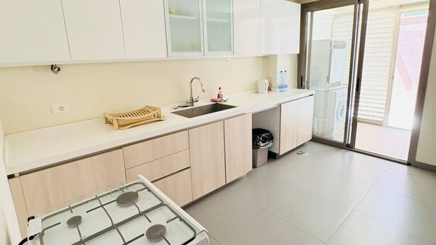 Una cocina moderna con armarios blancos, estufa a gas, un lavamanos y ventana con vista a un balcón.