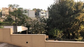 Una terraza en la azotea con un muro color beige, una barandilla metálica y un árbol con flores blancas.