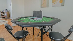 A roulette table with chairs around it, set in a room with wooden flooring and a white wall.