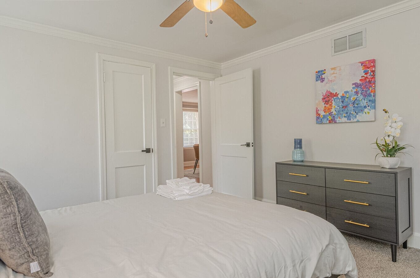 Une chambre à coucher comprenant un lit, une commode, un ventilateur de plafond et une porte donnant sur une autre pièce.