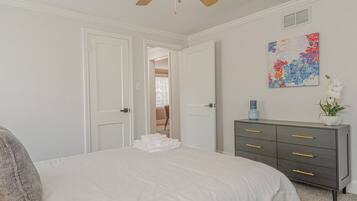 Une chambre à coucher comprenant un lit, une commode, un ventilateur de plafond et une porte donnant sur une autre pièce.