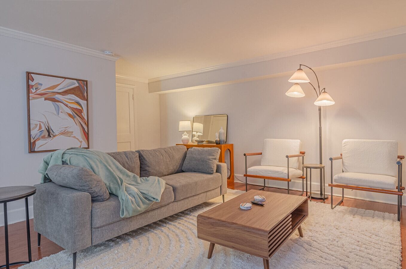 A modern living room with a grey sofa, two white armchairs, a wooden coffee table, and a floor lamp.