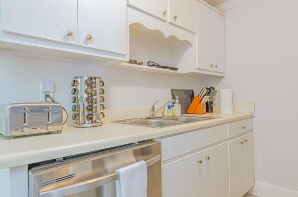 A kitchen with white cabinets, a stainless steel toaster, a coffee maker, and a sink. - MidTown Flats Suite B2 (Columbus)