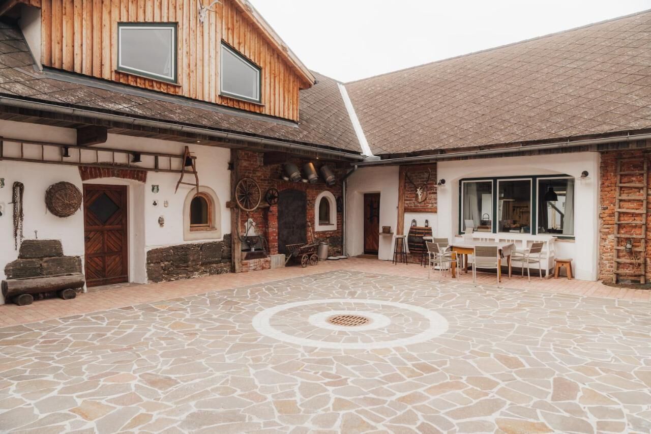 Un patio con suelo de piedra, un edificio de madera con techo inclinado y una pequeña zona de estar al aire libre.