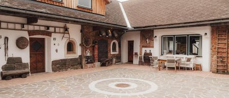 A courtyard with stone flooring, a wooden building with a sloped roof, and a small outdoor seating area.