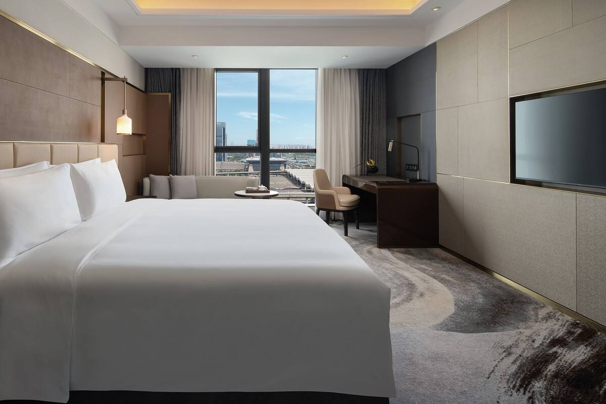 Habitación de hotel con una cama grande, un escritorio, una silla, un televisor y vistas de la ciudad.