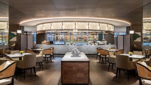 A modern restaurant with a central bar, seating around it, and a view of the kitchen. - Intercontinental Zhengzhou Zhengdong, by IHG (Zhengzhou)
