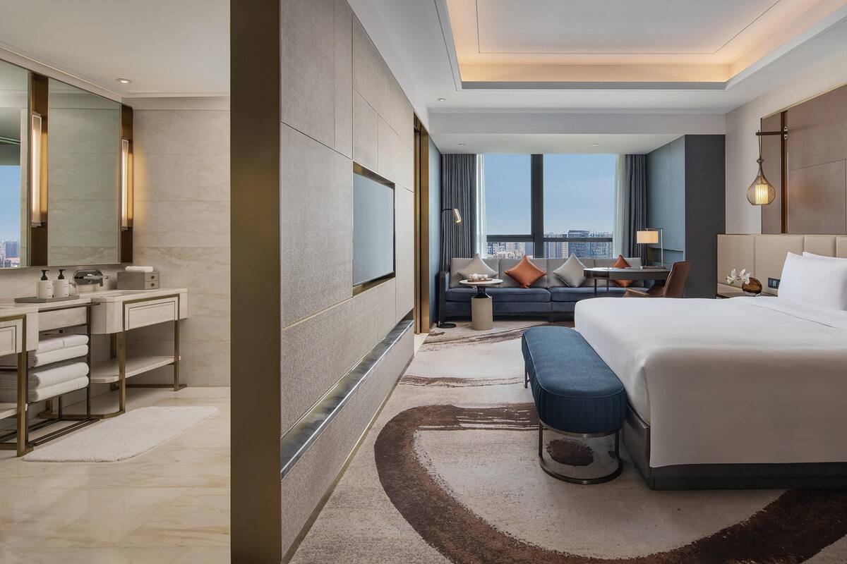 Una habitación de hotel moderna con una cama grande, un escritorio con una silla, un sofá y vistas a la ciudad.
