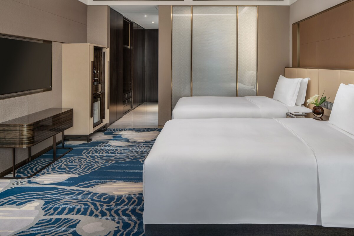 A hotel room with a large bed, a TV, a desk, and a patterned carpet.
