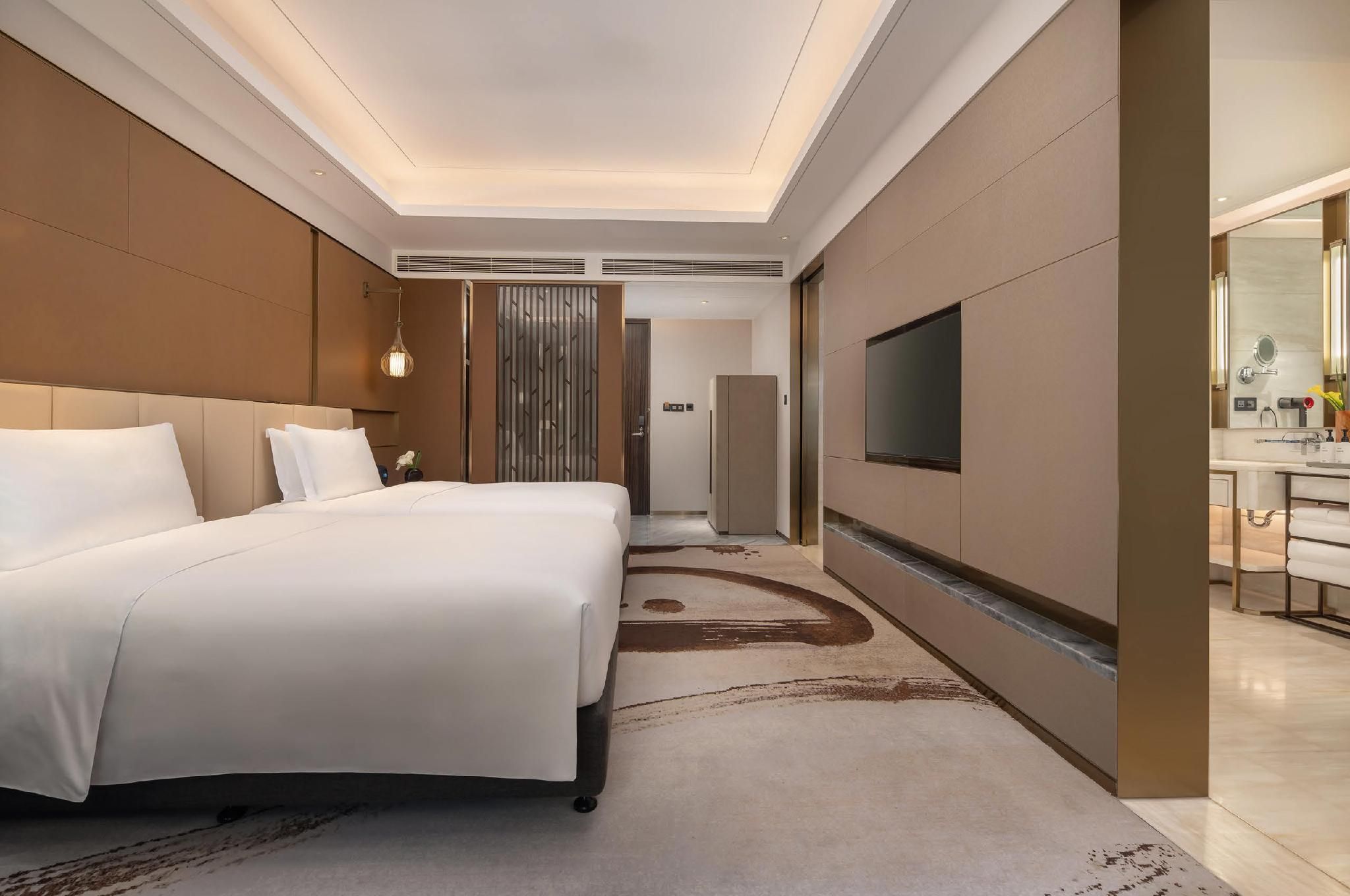 Een hotelkamer met een groot bed, een aan de muur bevestigde televisie en een badkamer met spiegel en wastafel.