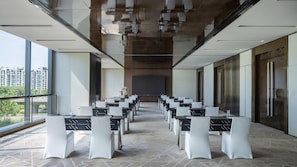 Een vergaderruimte met een lange tafel, stoelen, een groot scherm en uitzicht op gebouwen door grote ramen.