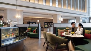 Eine moderne Hotelhalle mit Sitzbereichen, einem Empfangstisch und einer Glastheke.