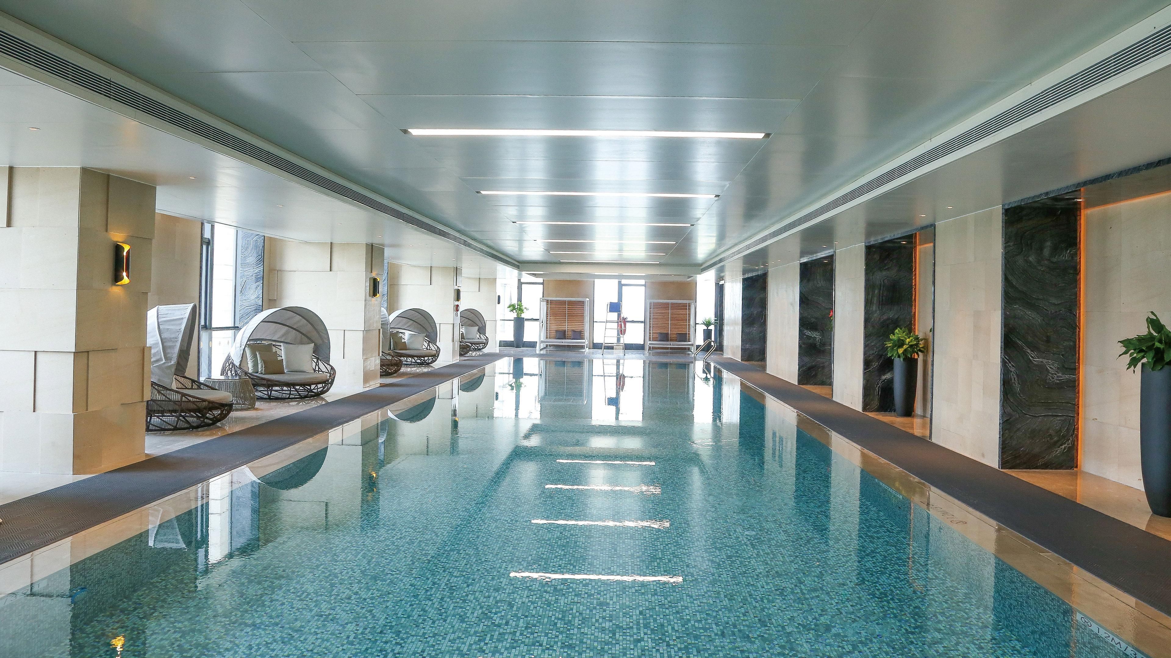 Una piscina interior larga con agua cristalina, rodeada de paredes con un diseño moderno y equipada con zonas de descanso a lo largo de los lados.